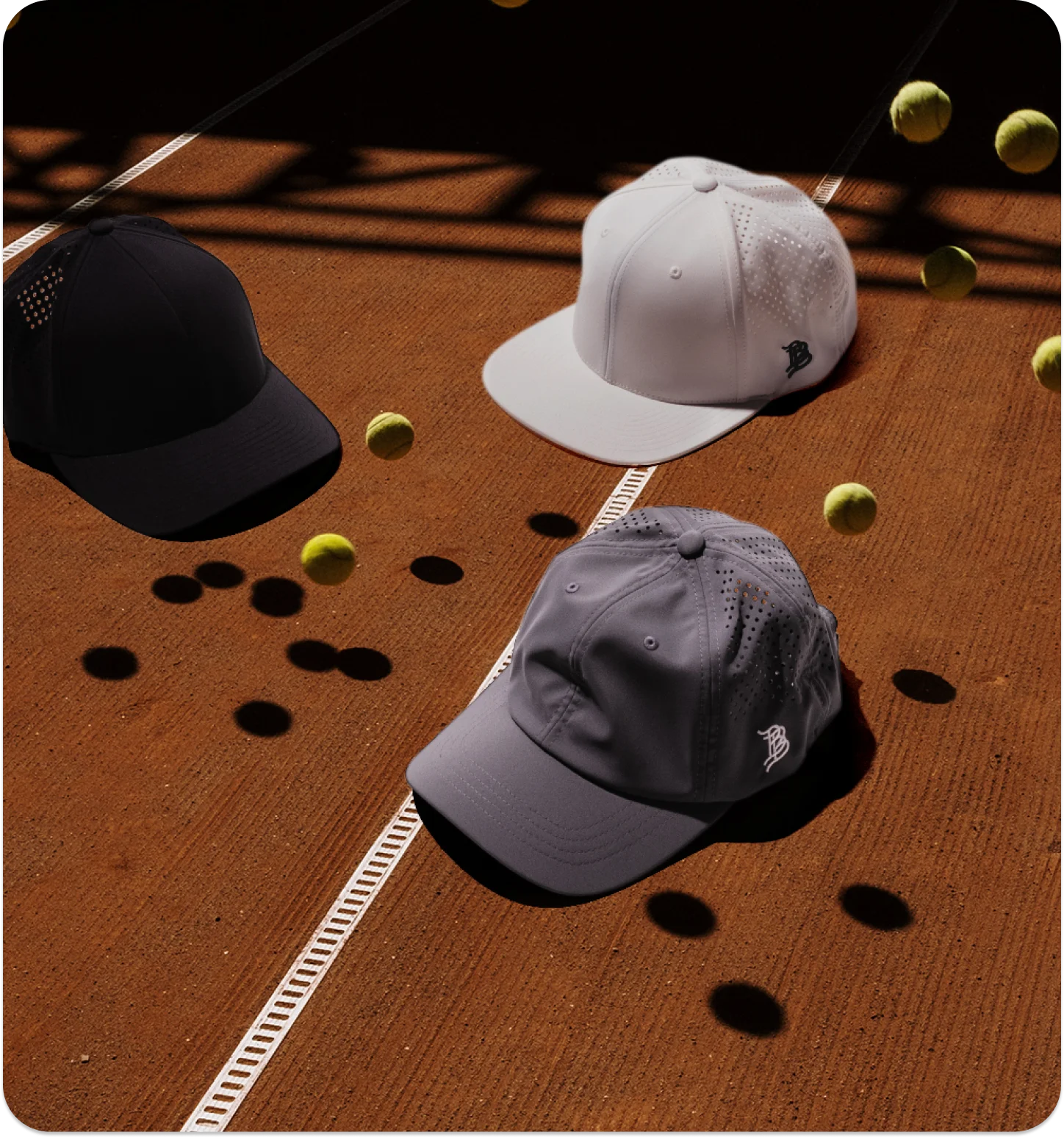 Three Branded Bills performance hats on a clay tennis court scattered with tennis balls.