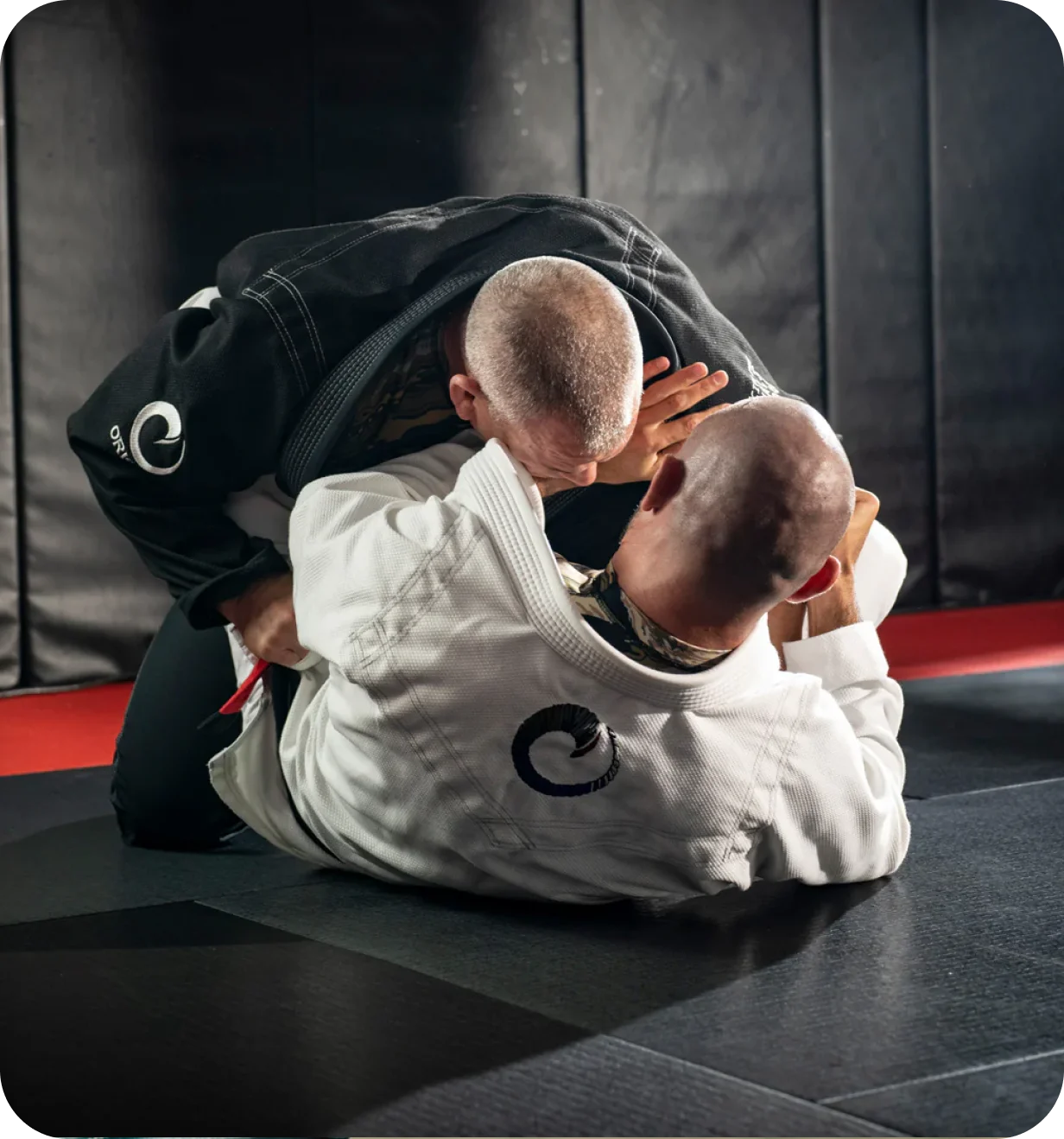 Two athletes in ORIGIN USA jiu-jitsu gis grappling on a training mat.