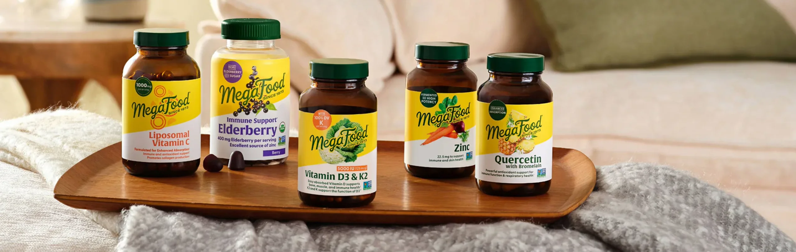 Five MegaFood supplement bottles lined up on a wooden tray in a cozy living room.