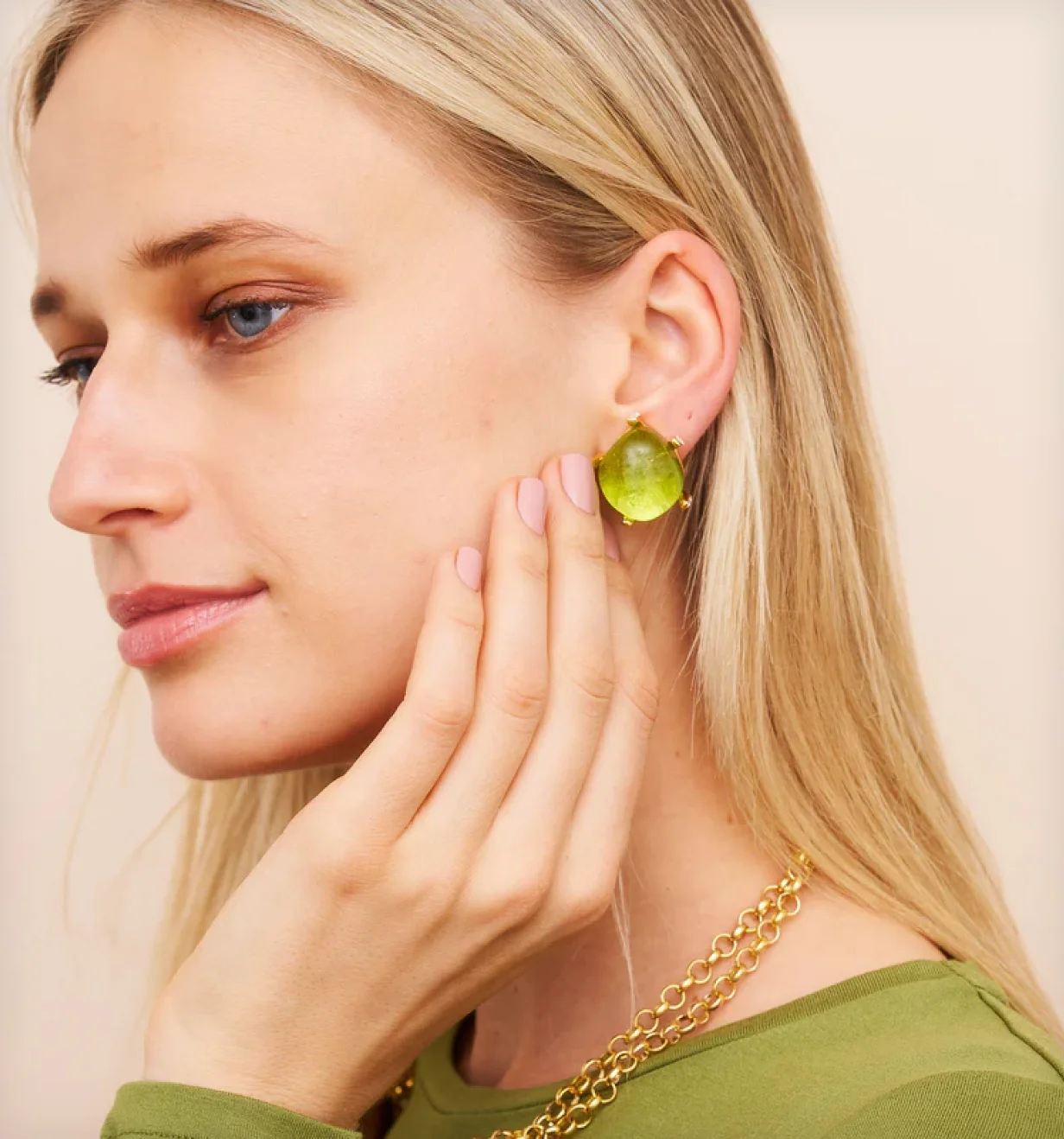Model wearing a Kenneth Jay Lane gold earring with a large green stone and gold chain necklaces.