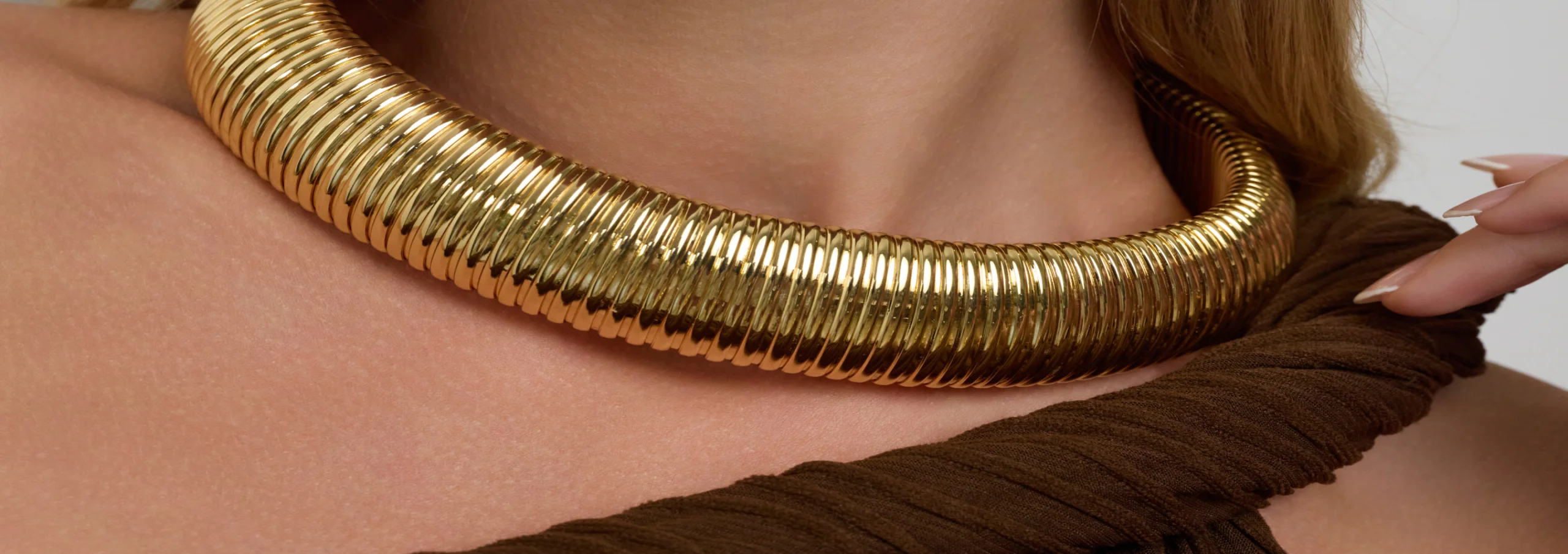 Close-up of a woman wearing a chunky ribbed gold Kenneth Jay Lane collar necklace.