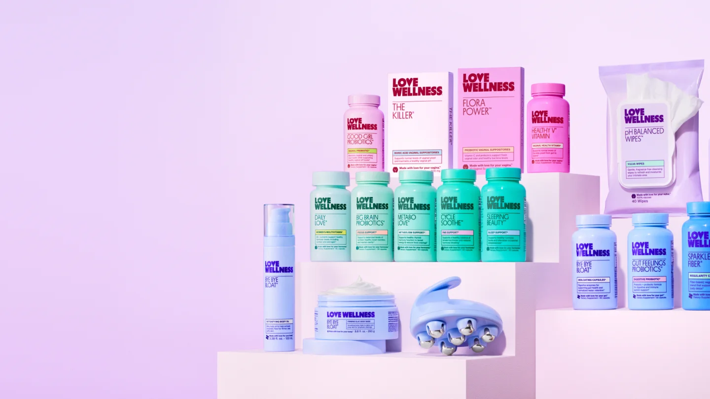 Full line of colorful Love Wellness supplements and body care products on pastel pedestals.