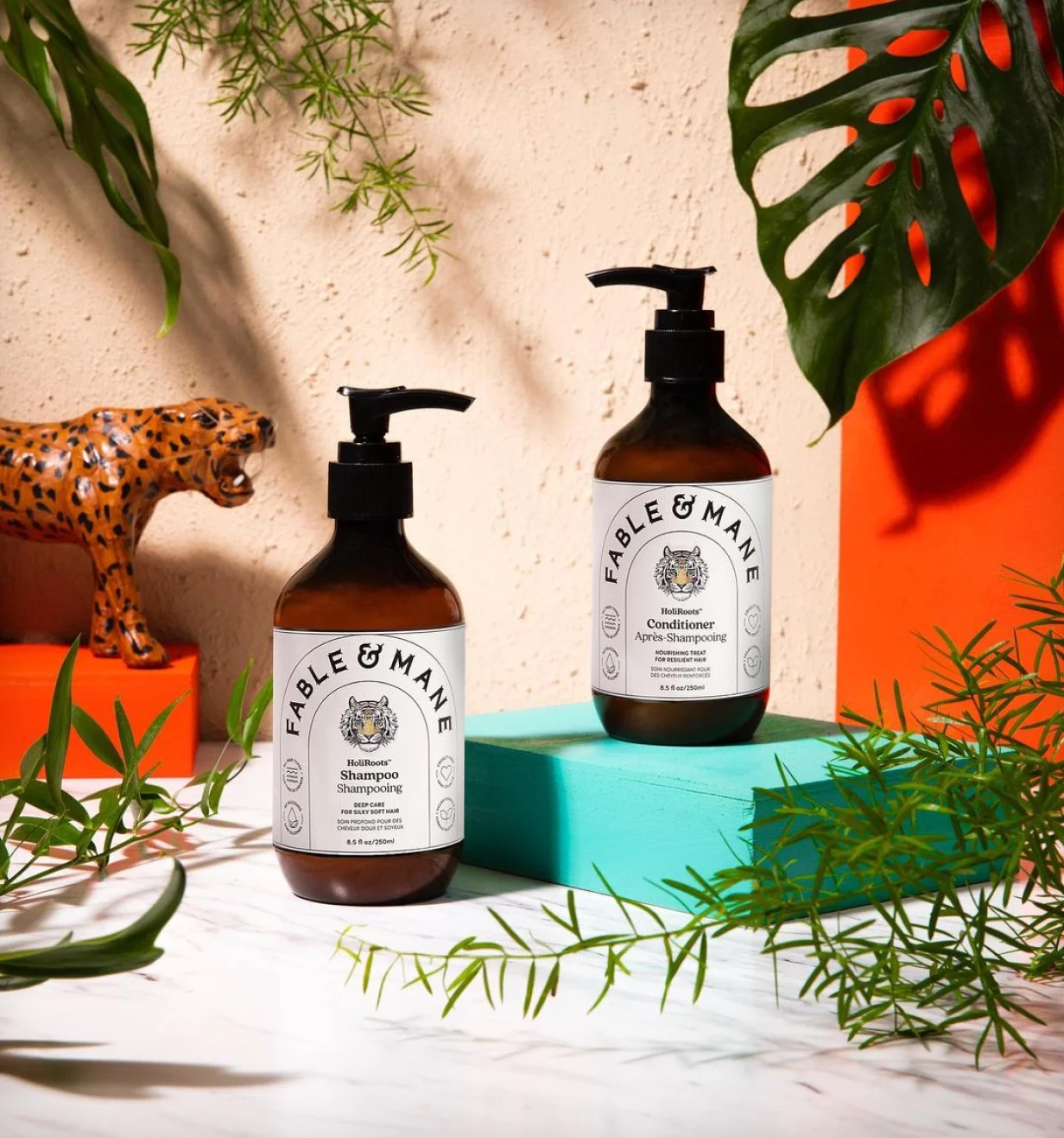 Fable & Mane lifestyle photo of HoliRoots shampoo and conditioner bottles among tropical plants.