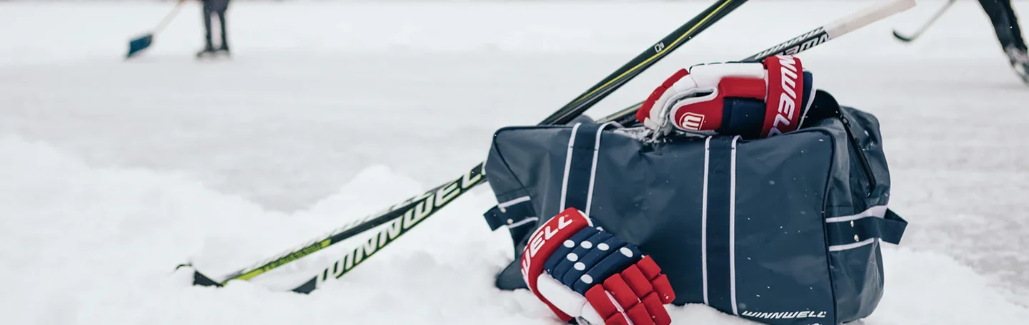 Winnwell hockey gloves, sticks, and equipment bag resting on the snow of an outdoor rink.