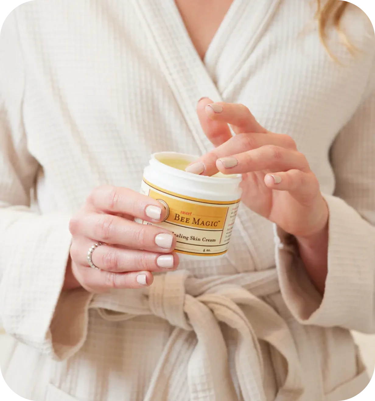 Sweet Bee lifestyle photo of a woman in a robe using Sweet Bee Magic healing skin cream.