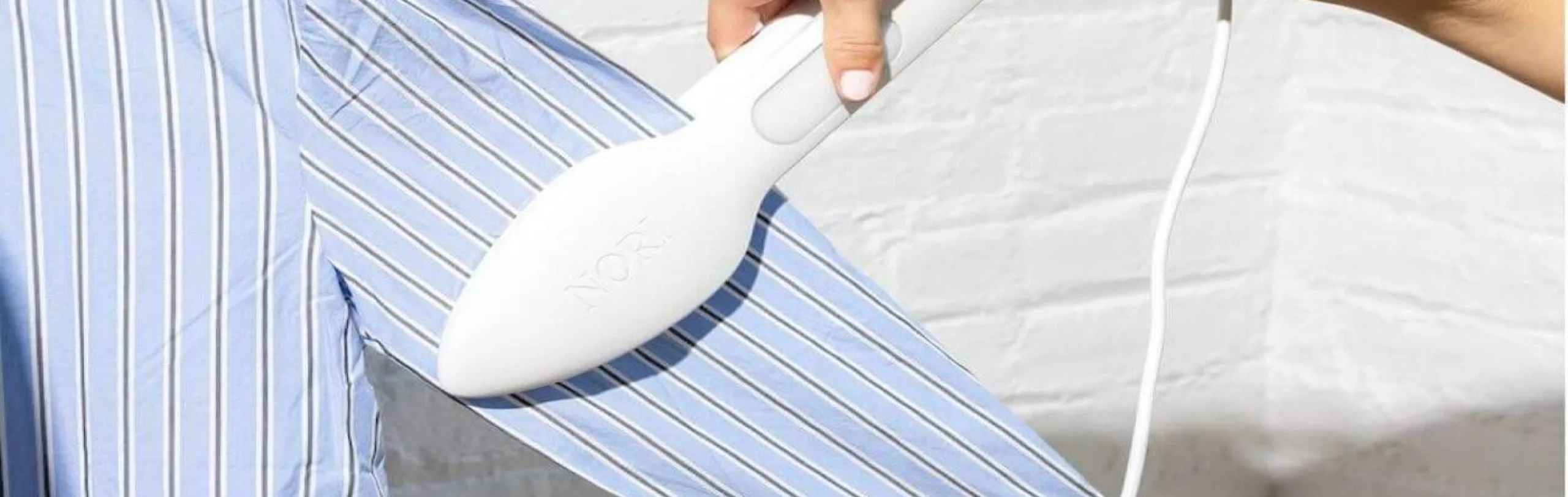 Hand smoothing a white Nori press iron over a blue striped shirt.