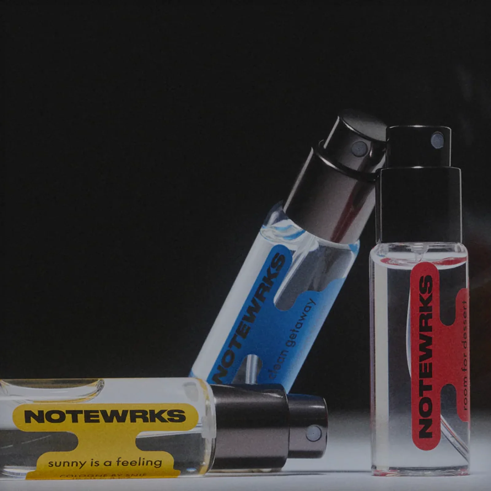 Three Notewrks by Snif cologne sprays with yellow, blue, and red labels on a dark background.