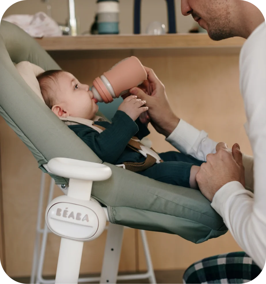 Béaba lifestyle photo of a parent bottle-feeding a baby seated in a Béaba bouncer.