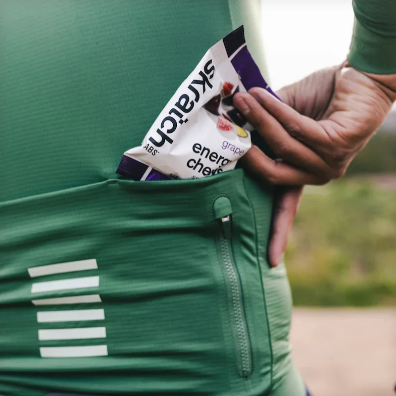 Cyclist pulling a pack of Skratch Labs energy chews from a green jersey pocket.