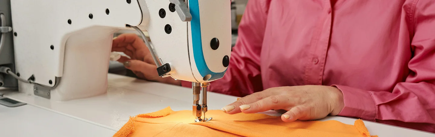 Garment worker guiding orange fabric through an industrial sewing machine.