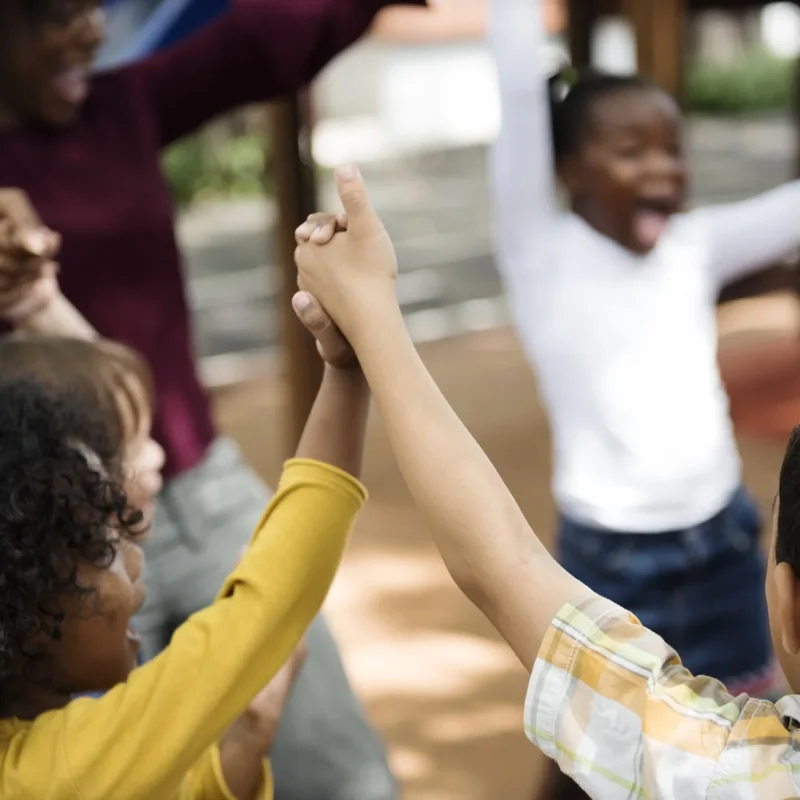 Children on a playground cheering and raising joined hands for Circle of Security International.