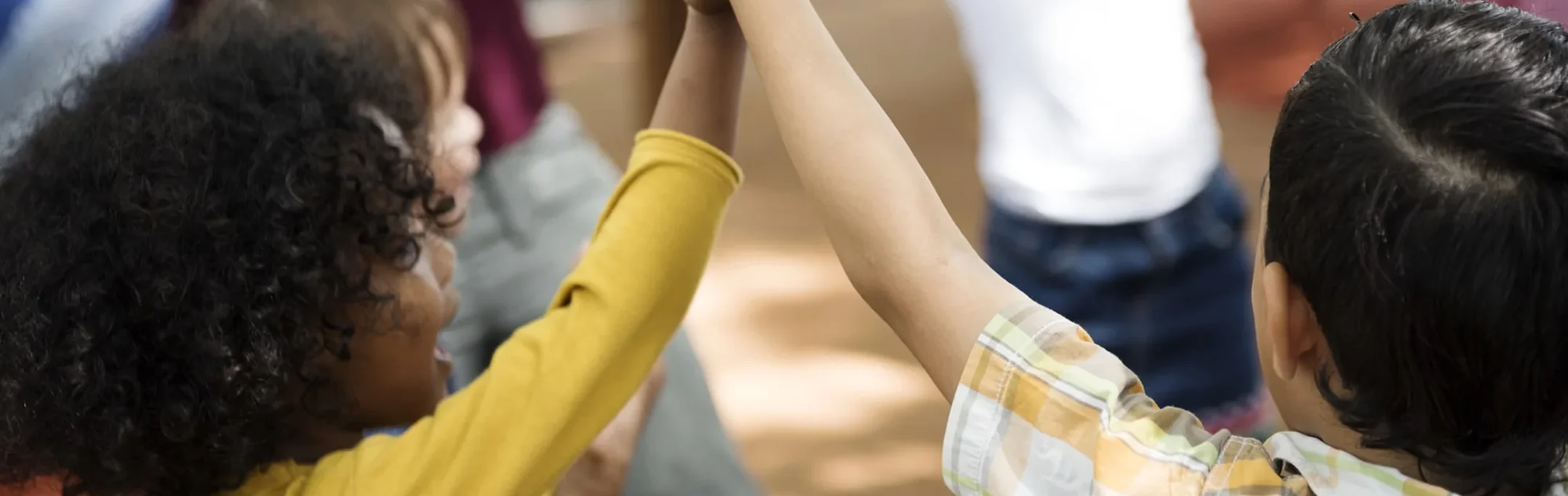 Two young children reaching up to share a high five outdoors.
