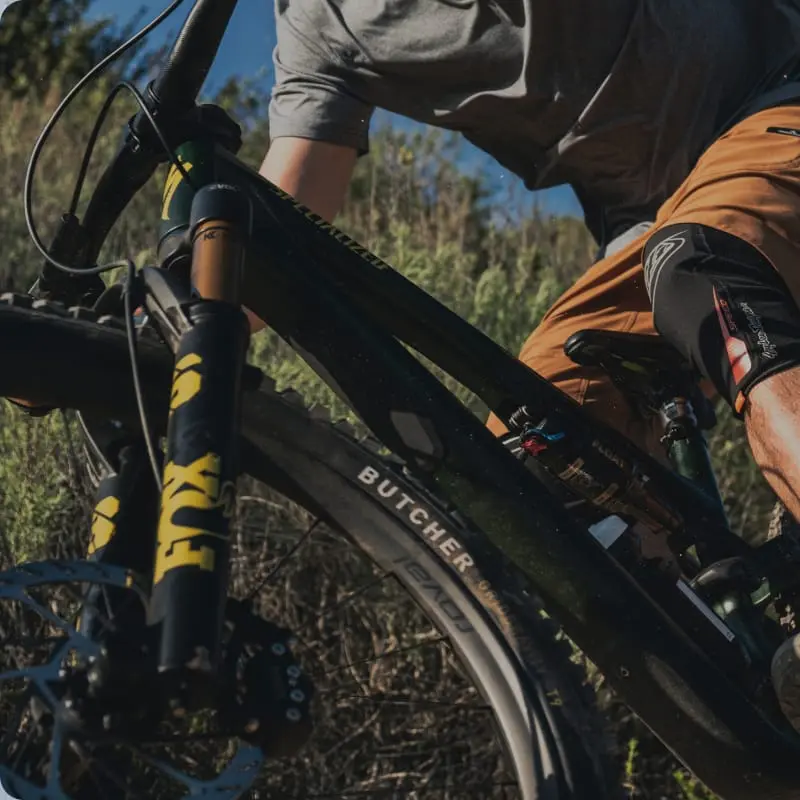Close-up of a mountain biker riding a full-suspension bike with a Fox fork along a dusty trail.