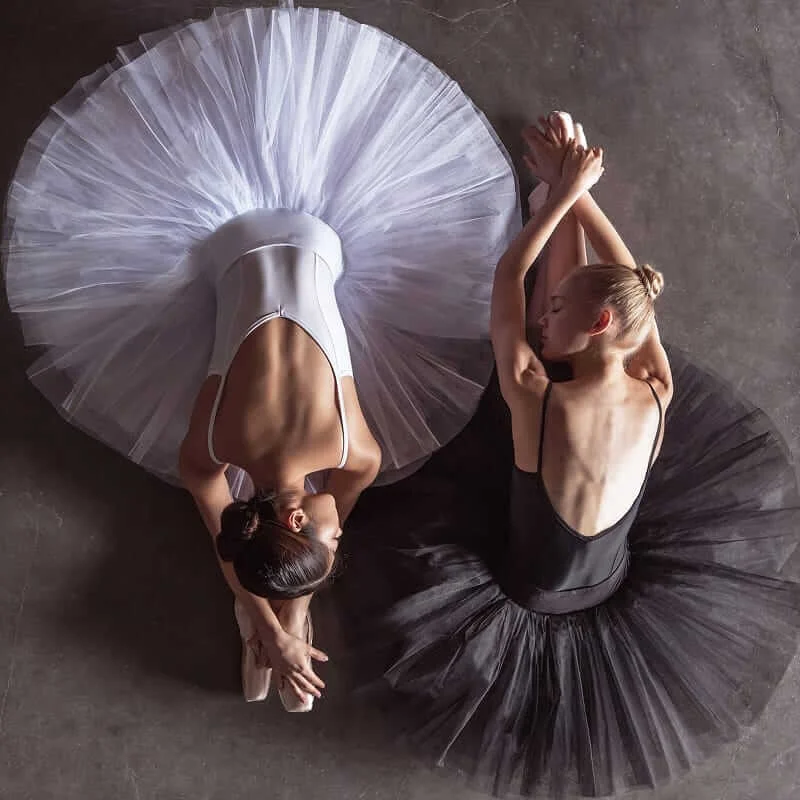 Overhead view of two ballerinas in white and black tutus resting on a studio floor.