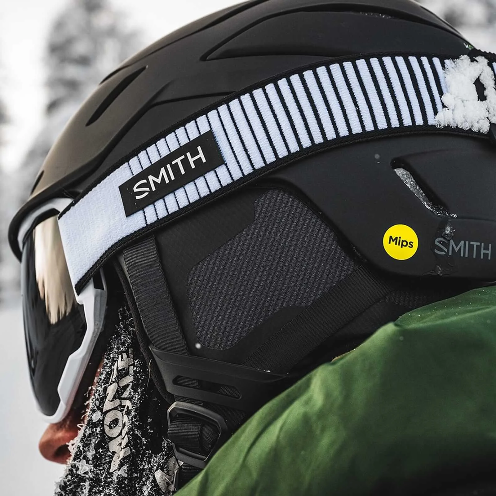 Close-up of a skier wearing a black Smith Mips helmet and Smith goggles with a snow-dusted strap.