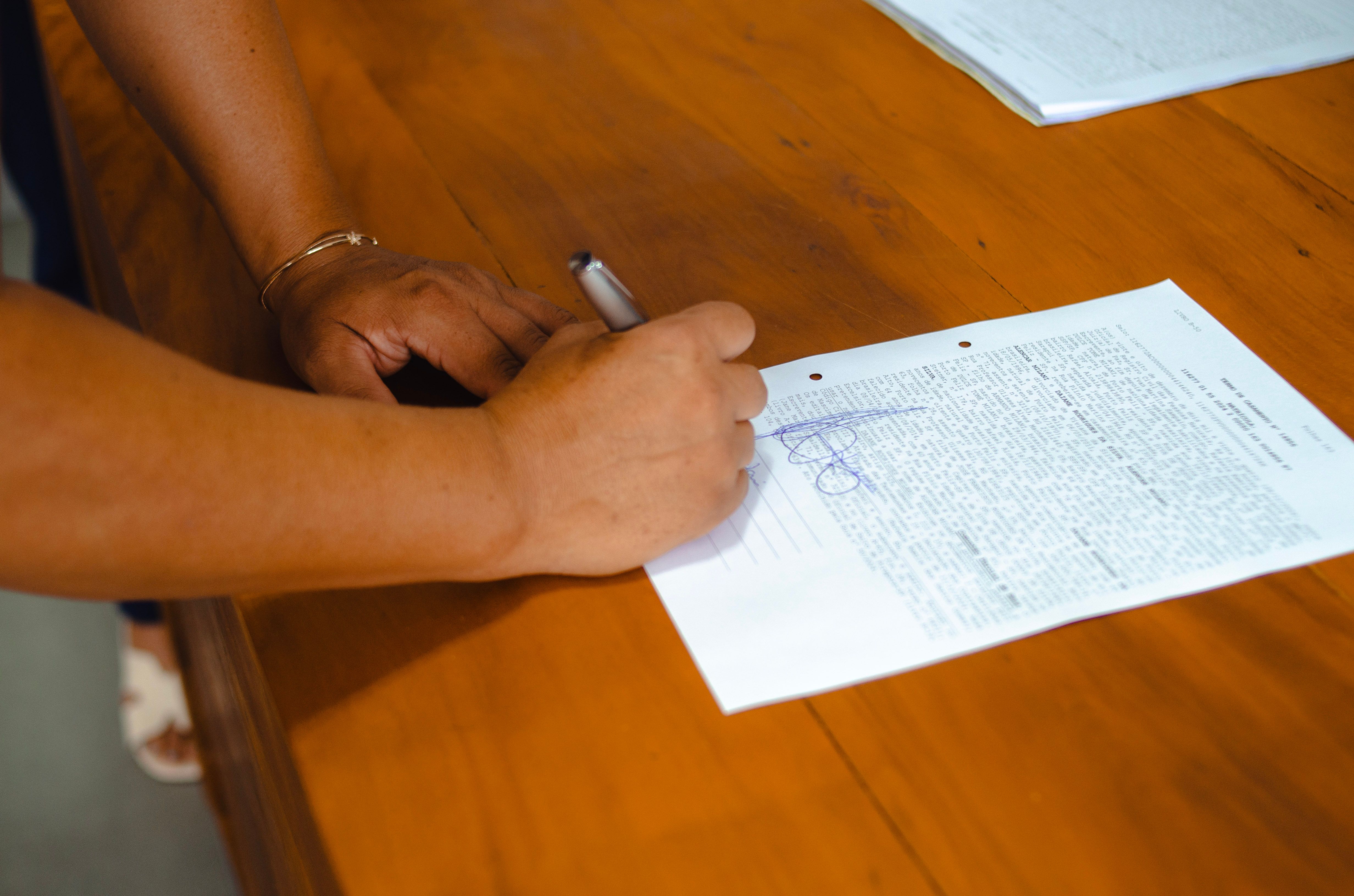 Hands signing a legal document on a wooden table