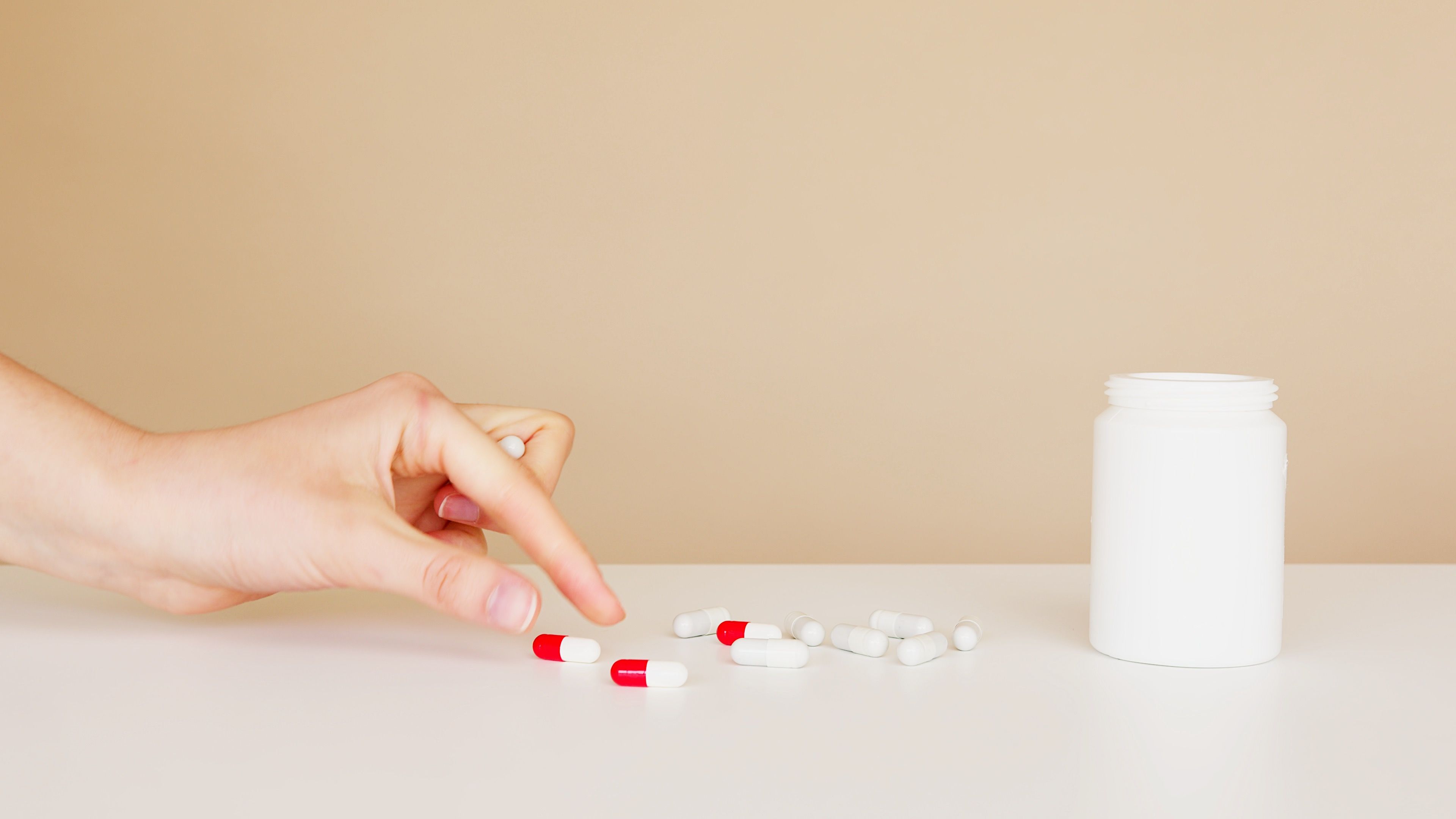 Hand reaching for pills beside an open medicine bottle