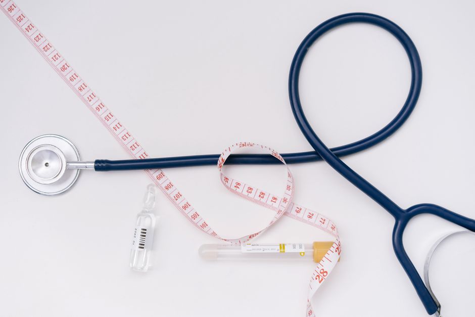 A stethoscope, ampoule, and tape measure on a white background symbolize healthcare essentials.