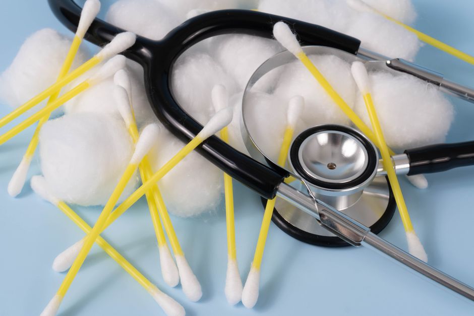 Close-up of a stethoscope with cotton balls and earbuds on a blue background.