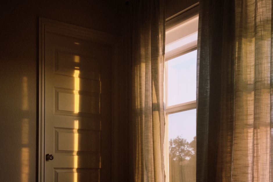 Warm sunlight filters through curtains, casting shadows in a cozy room corner.
