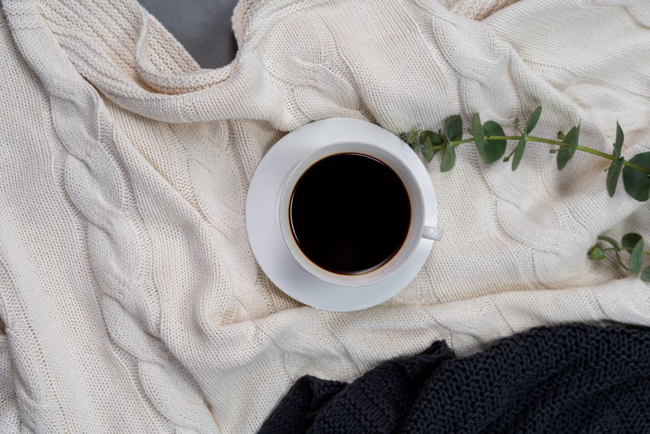 A cozy setup featuring black coffee on a cable knit blanket with green accents, perfect for leisure moments.