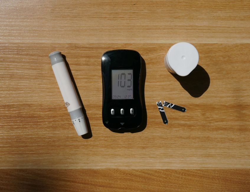 A diabetes testing kit with glucose meter, lancet pen, and test strips on a wooden surface.