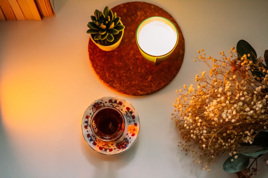 A warm and inviting scene with a tea cup, candle, succulent, and dried flowers on a table.