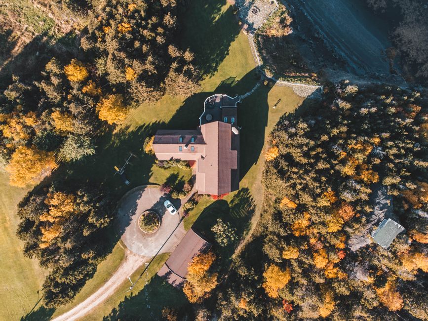 Aerial shot showcasing a countryside house surrounded by vibrant autumn trees and lush green landscapes.