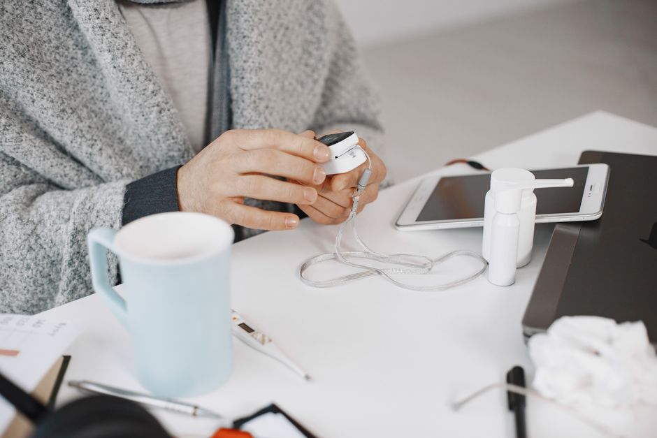 Close-up of hands using a health device at a desk with electronic gadgets and a cup.