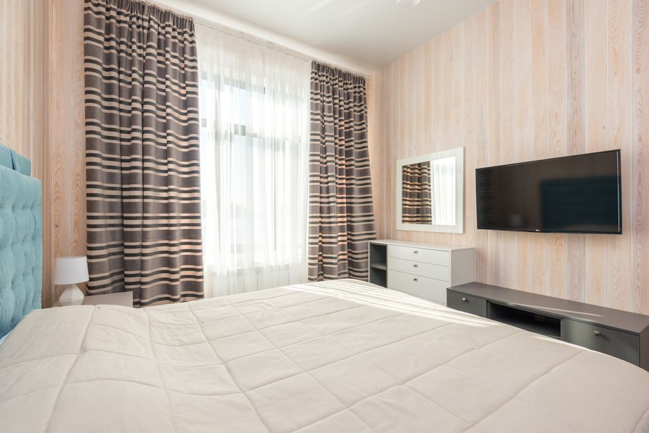 Contemporary bedroom with striped curtains, TV, and elegant furnishings.