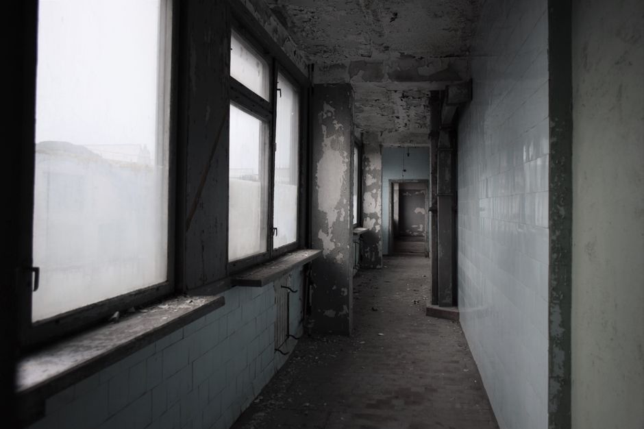Eerie hallway in an abandoned building with decaying walls and muted lighting.
