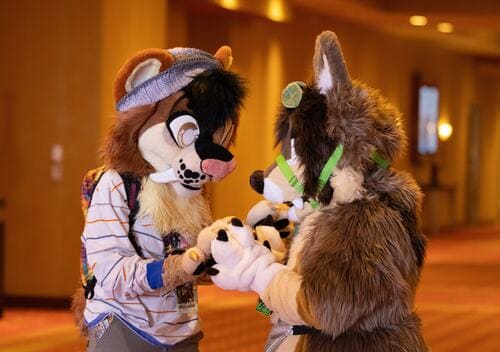 Two mammal fursuiters holding hands.