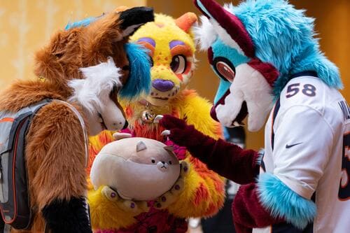 Three fursuiters petting a stuffed animal.