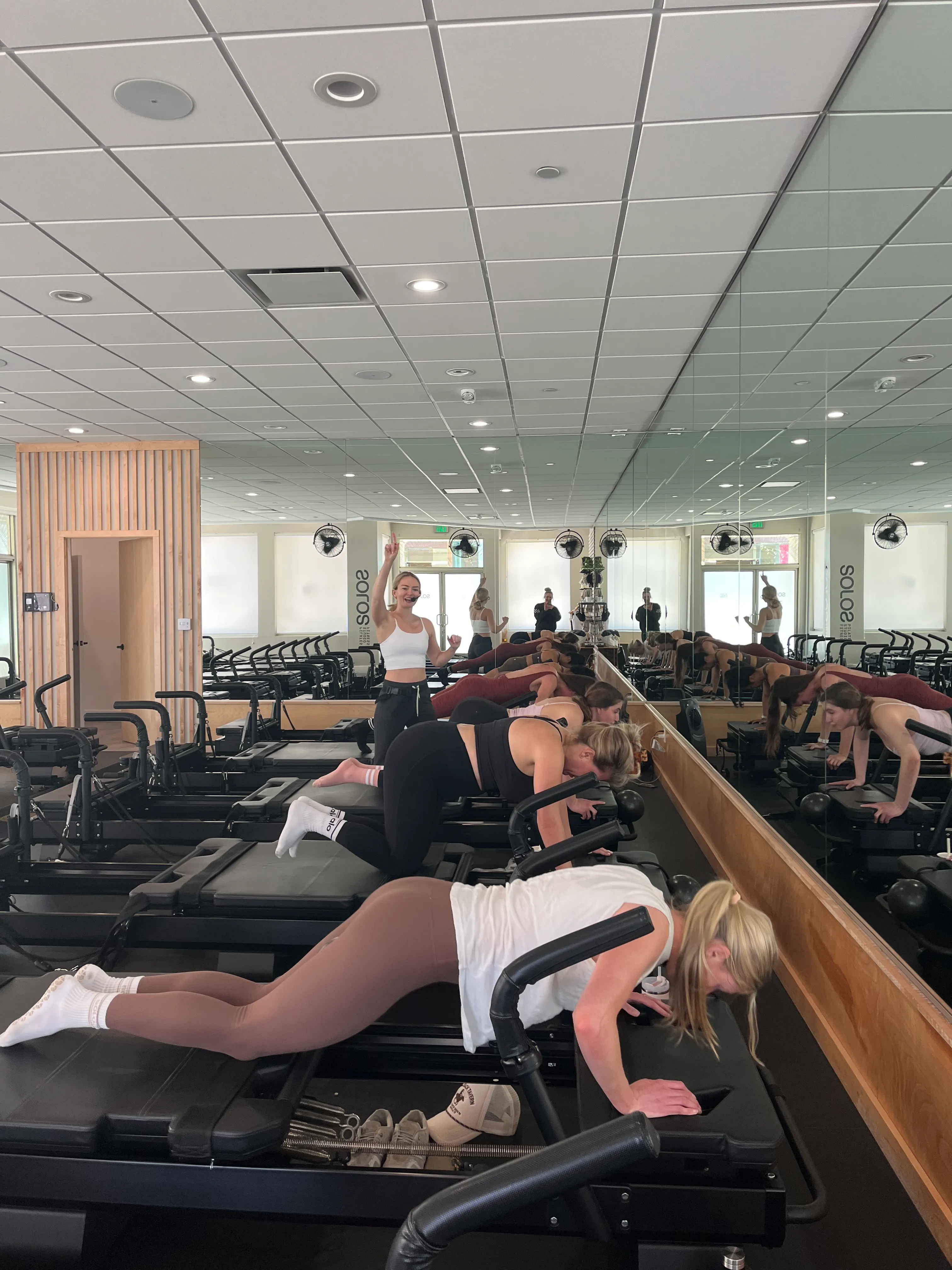 Group fitness class with women performing exercises on Pilates reformer machines in front of a large mirror.