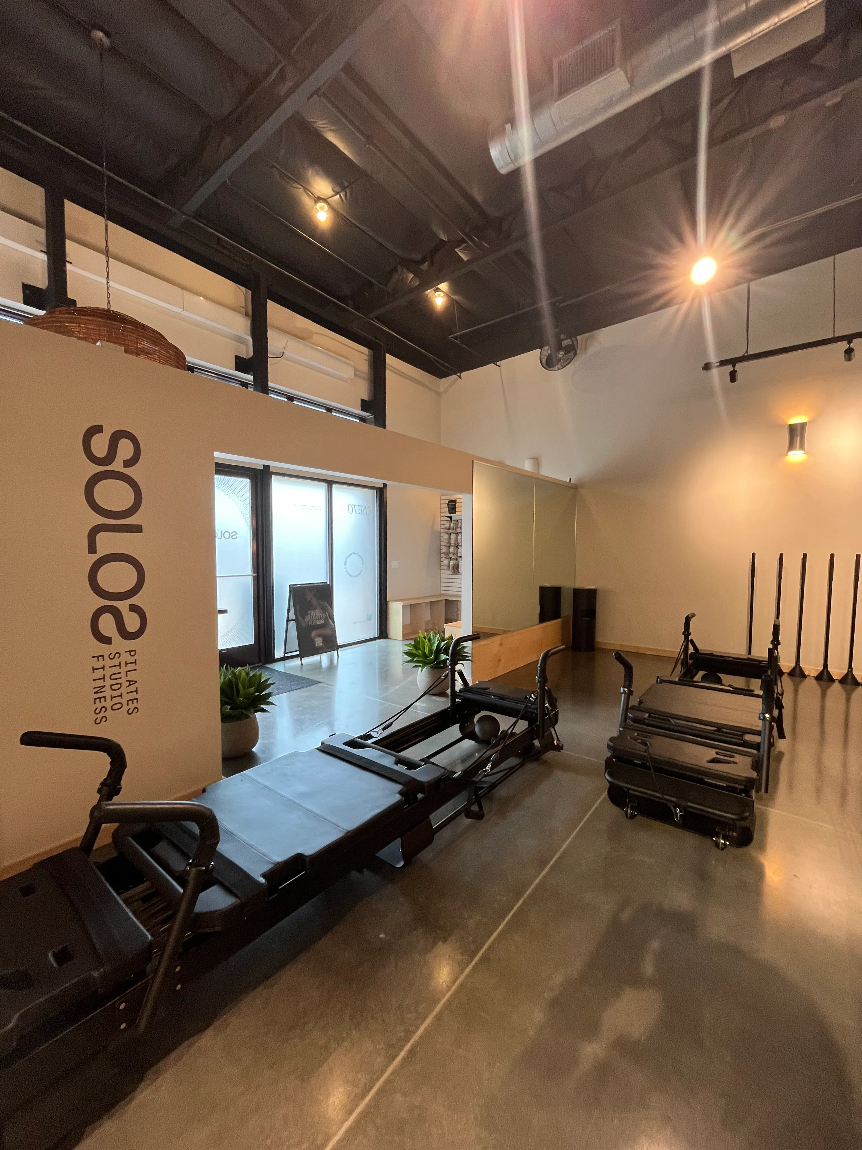Indoor Pilates studio with reformer machines, polished concrete floors, and light beige walls with the sign 'SOLOS Pilates Studio Fitness'.