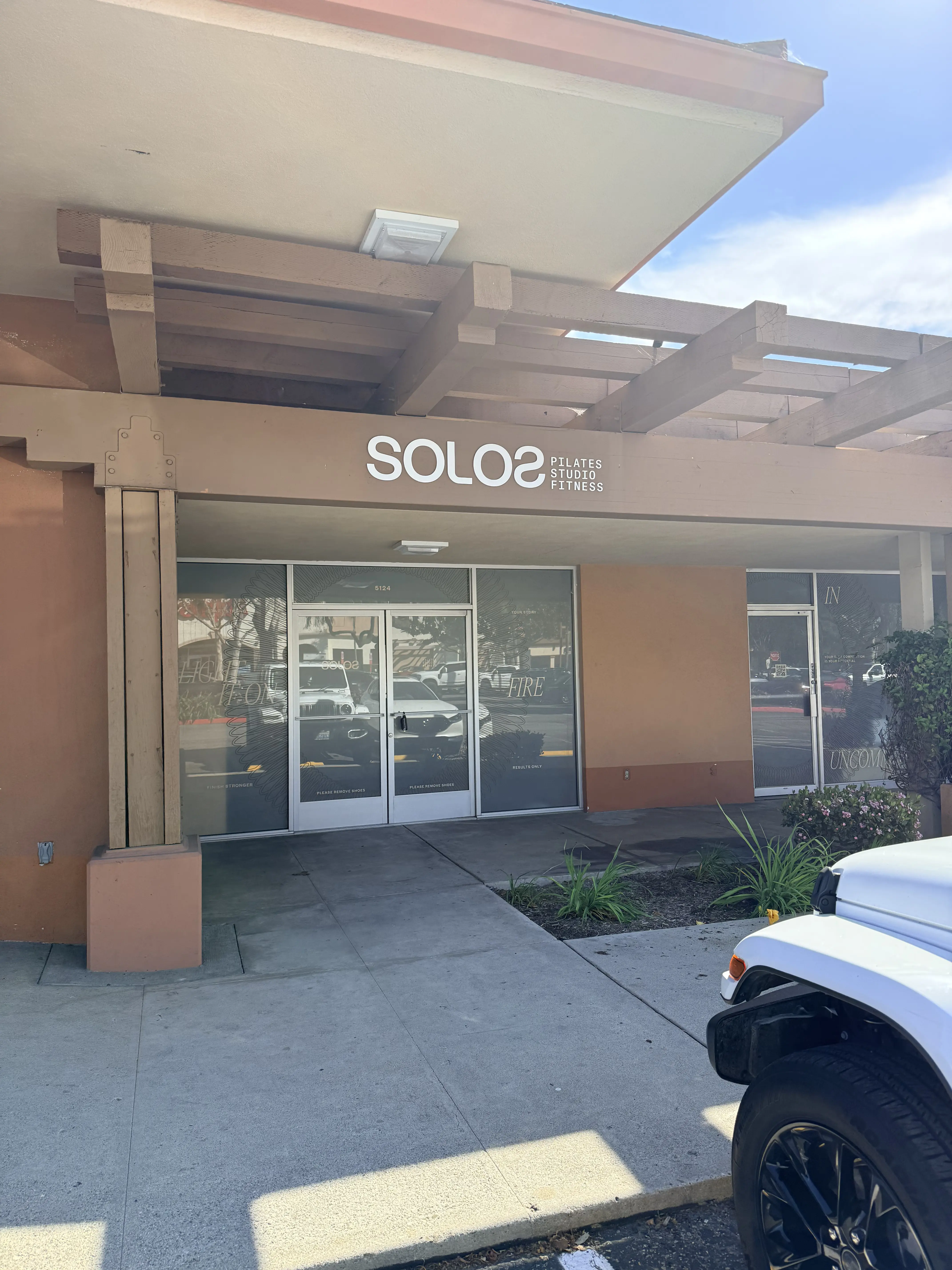 Entrance to a Pilates studio named SOLOS with glass double doors and a visible white car parked nearby.