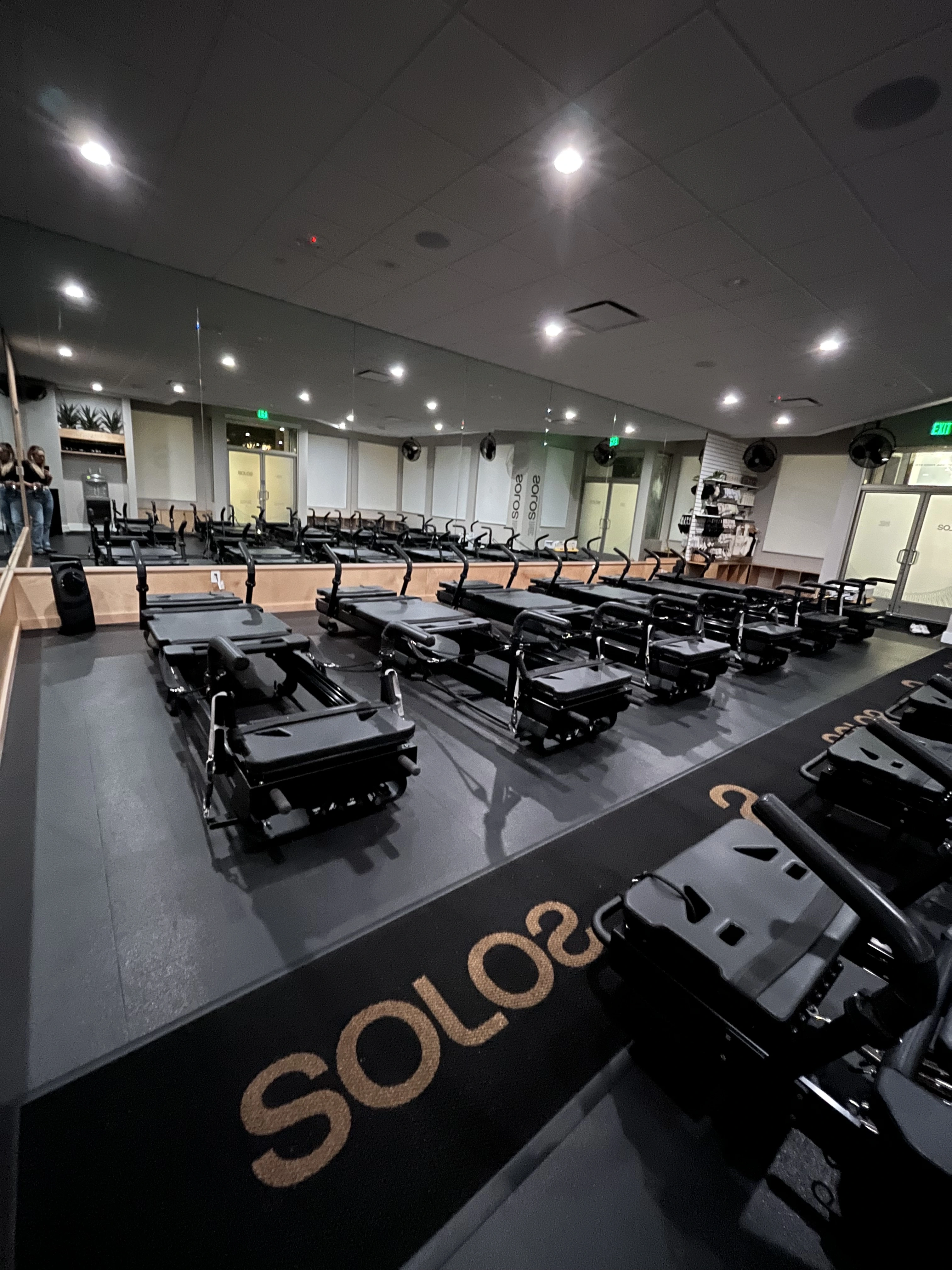 Exercise studio with rows of black Pilates reformer machines on a black floor mat labeled SOLO.