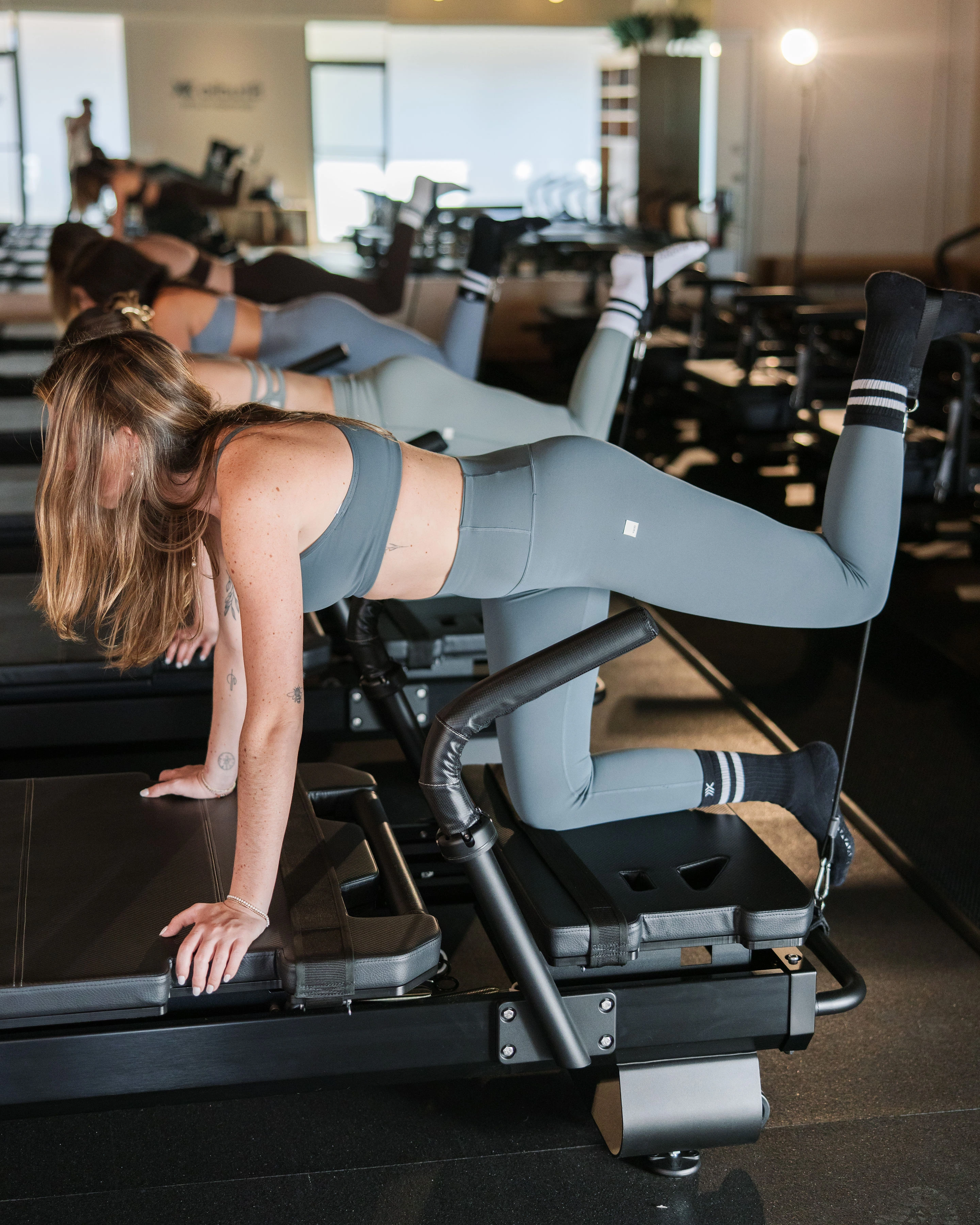 Women exercising on Pilates reformer machines in a bright fitness studio.