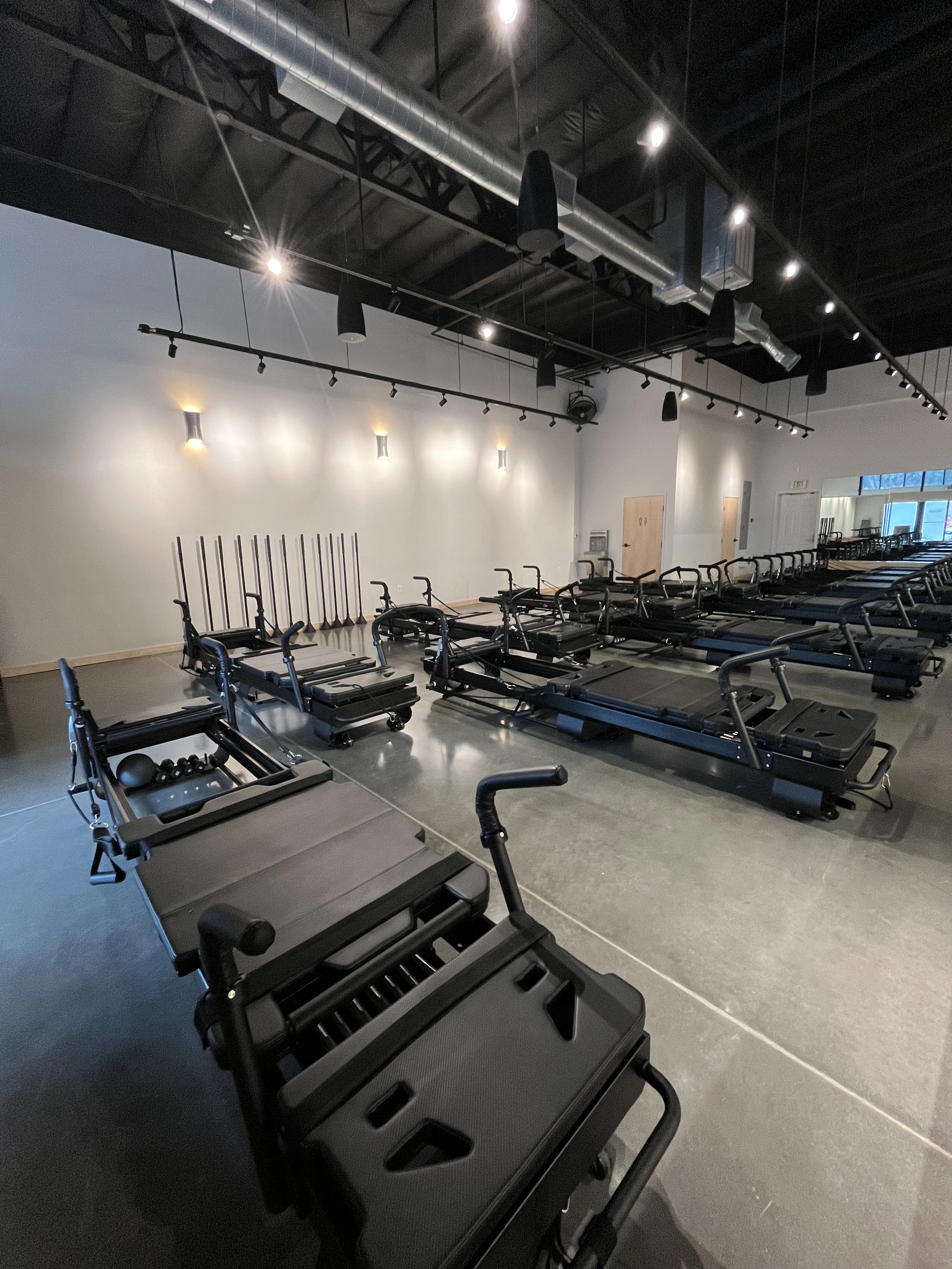 Empty Pilates reformer machines lined up on a polished concrete floor inside a bright fitness studio.