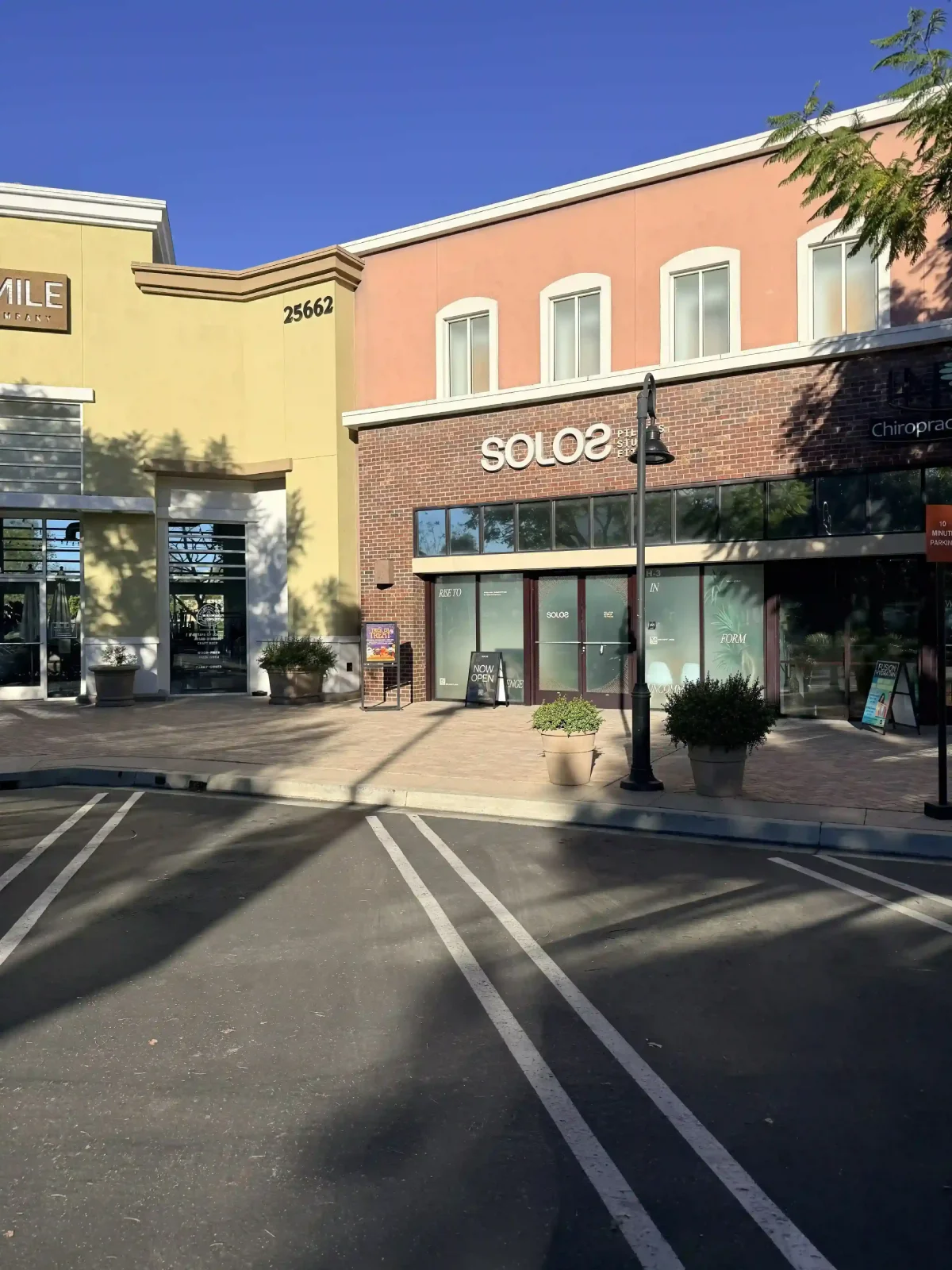Empty parking spaces in front of a retail area with a yellow building and Solo2 Pilates studio.