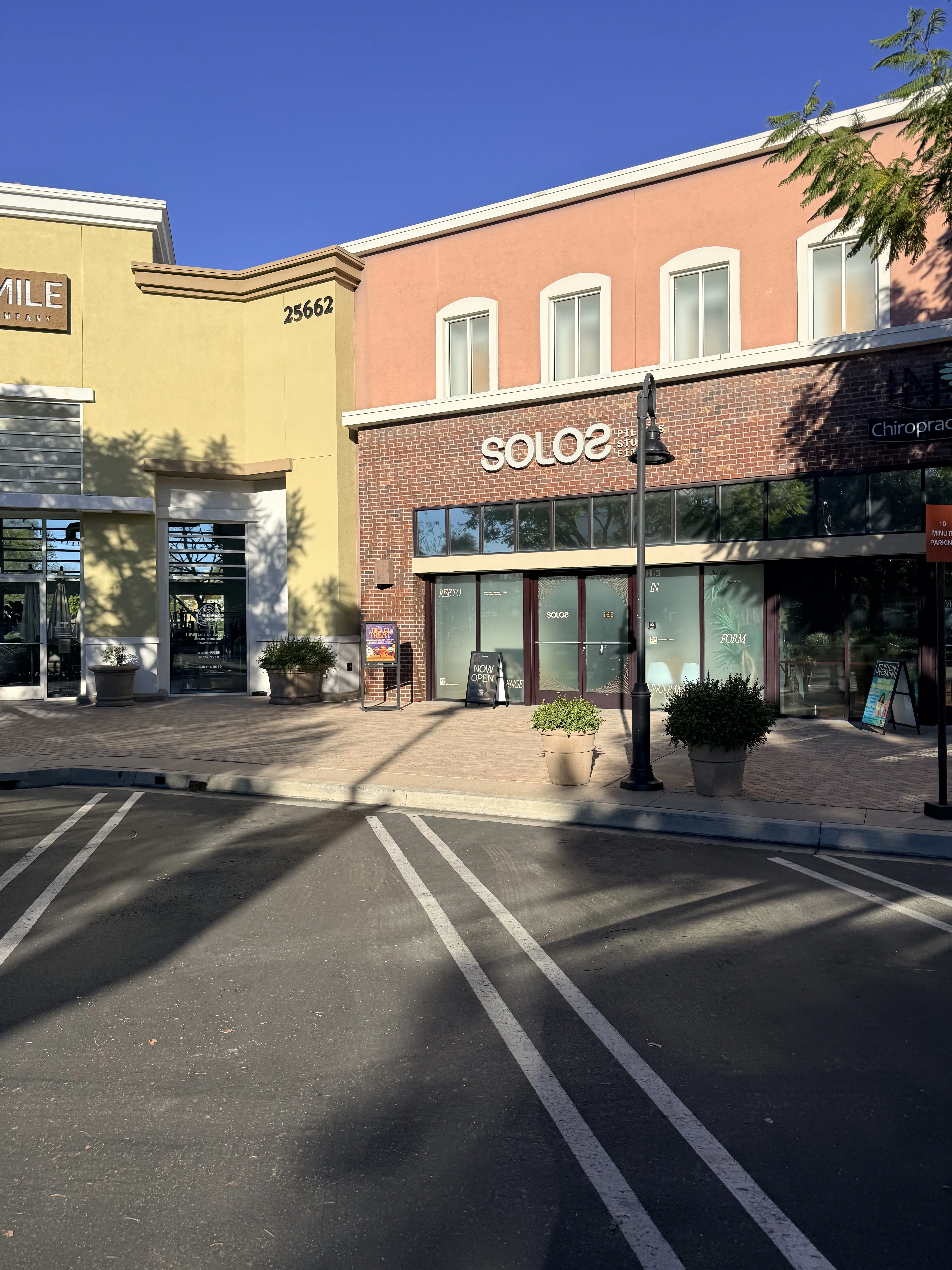 Empty parking spaces and building storefronts under clear blue sky with shadows from nearby trees.