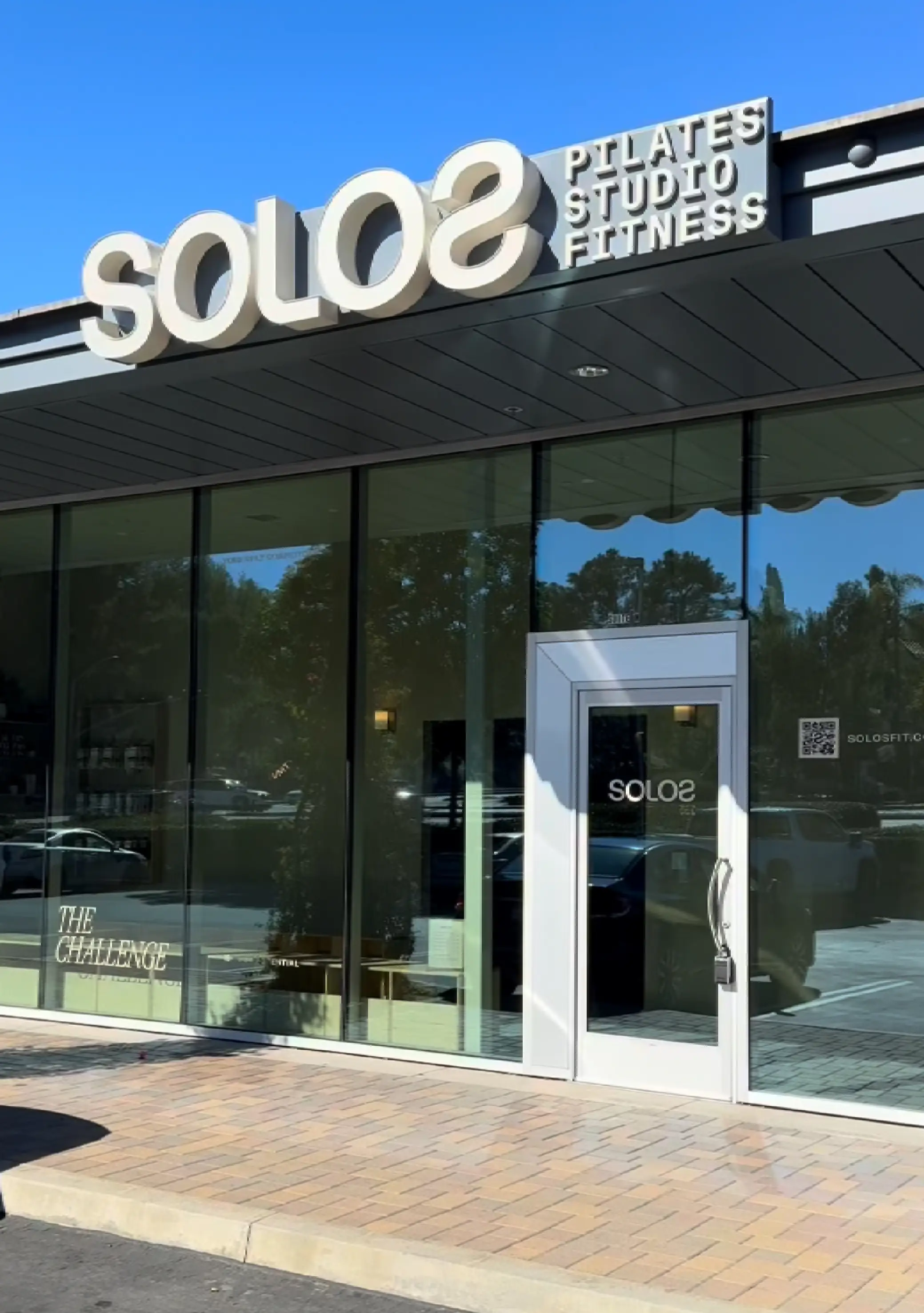 Exterior front of a Pilates studio named SOLOS with glass windows and door under a clear blue sky.