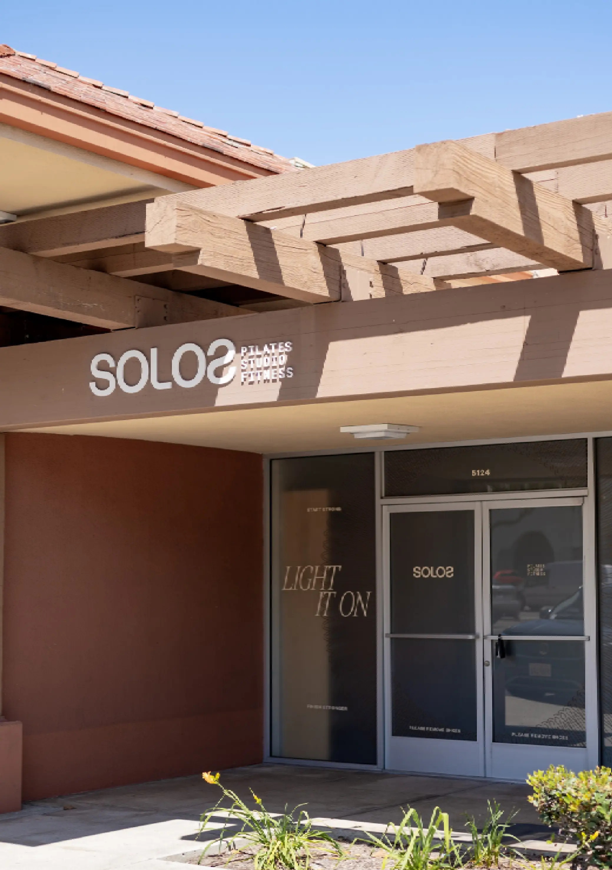 Entrance to Solo Pilates Studio Fitness with wooden pergola and glass doors featuring motivational text.
