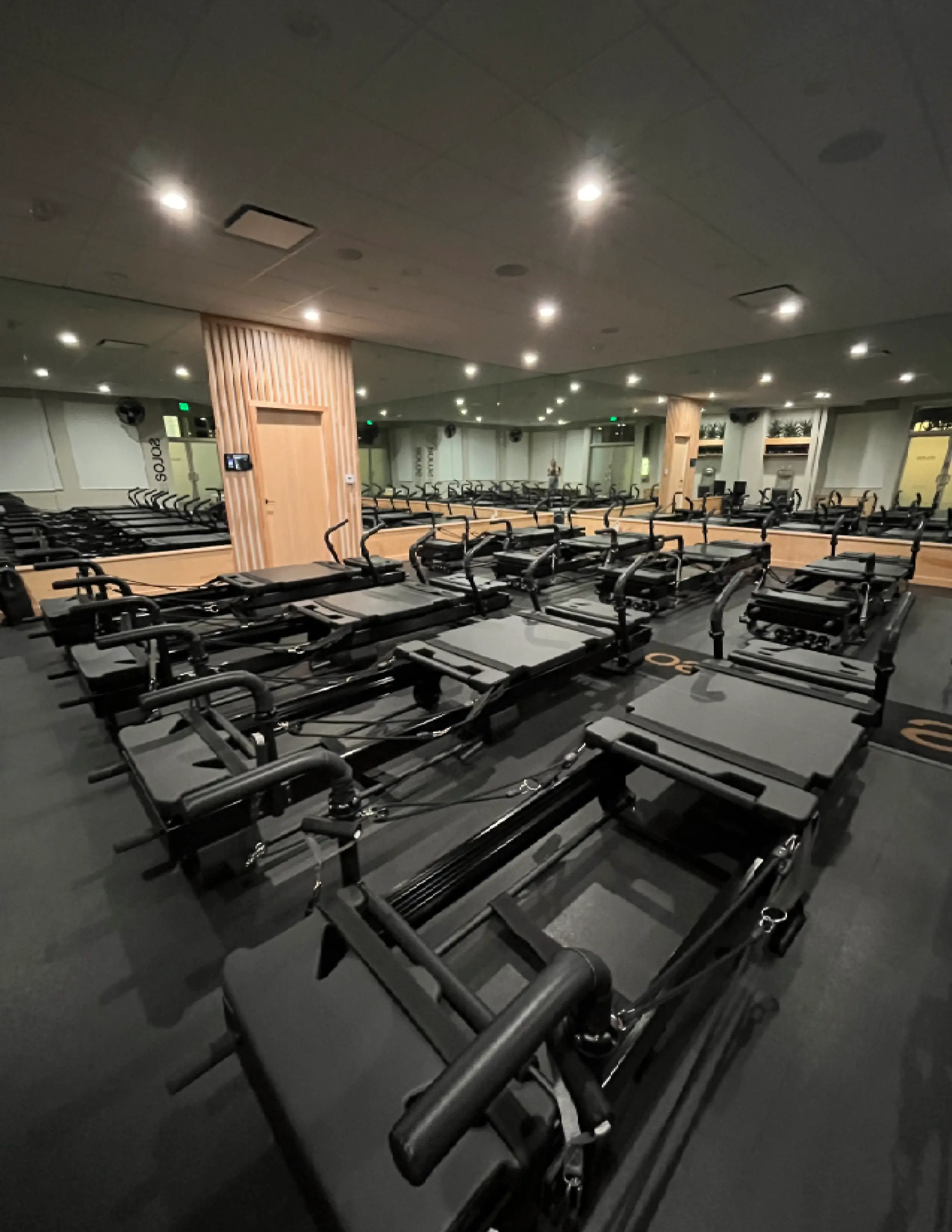 Empty Pilates reformer machines lined up in a well-lit fitness studio with mirrored walls and wood accents.