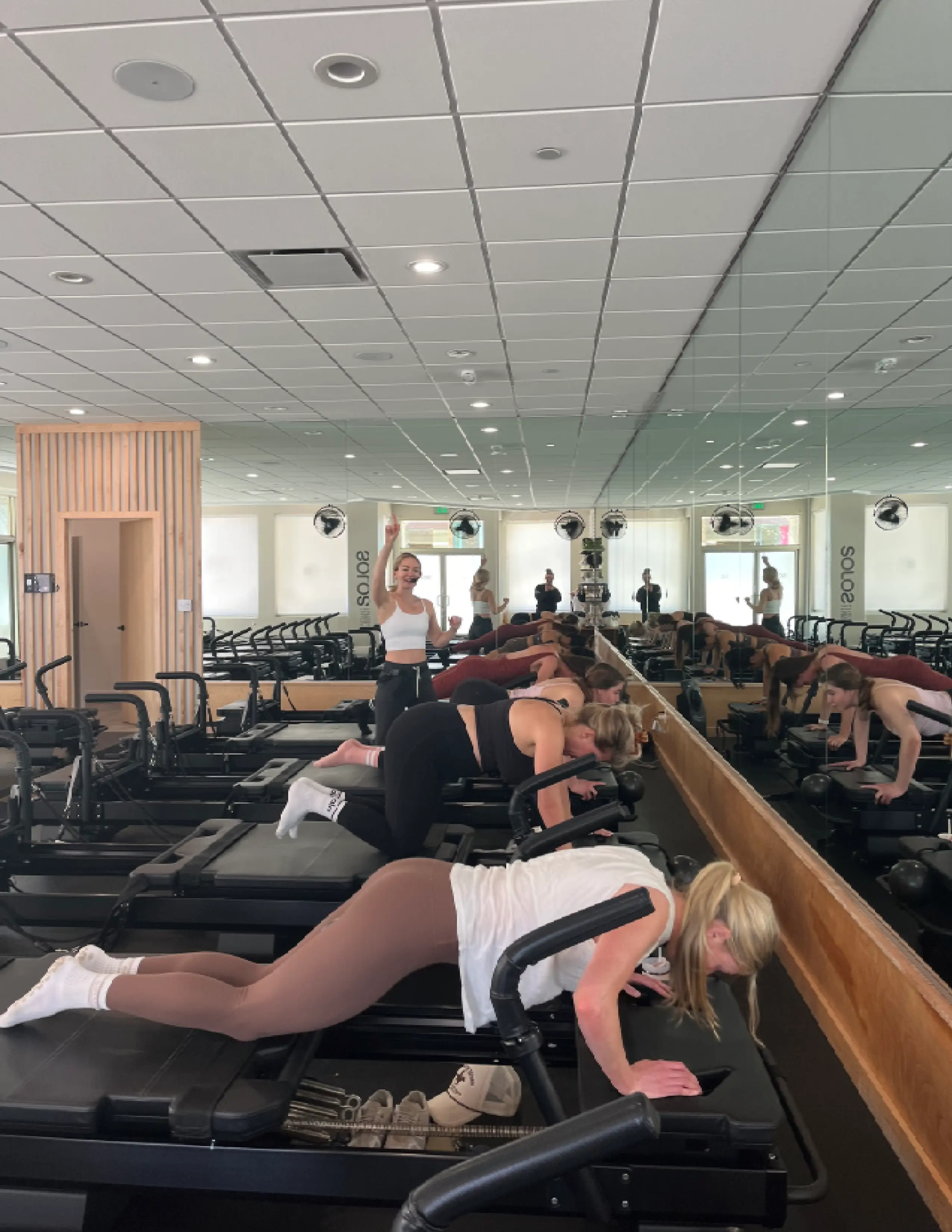 Four women exercising on reformer machines in a mirrored Pilates studio with an instructor in front.