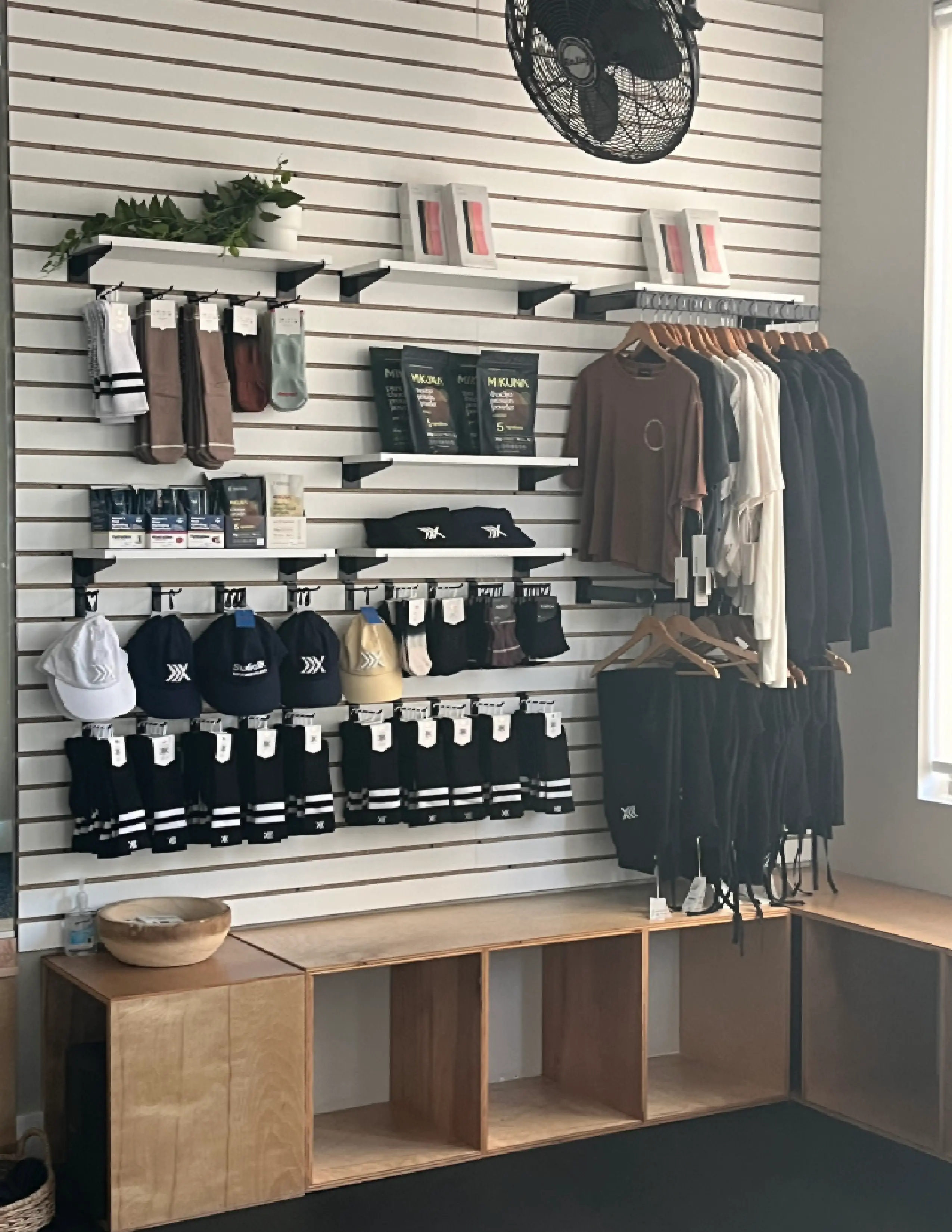 Retail display with hats, socks, shirts, and accessories on wall shelves and hangers near a wooden bench.