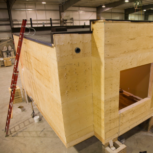 Prefabricated timber building module inside a factory, showing windows and service openings before installation