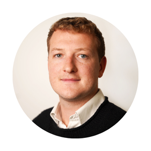 Portrait of a man with short light brown hair wearing a white shirt and dark jumper, shown in a circular profile photo.