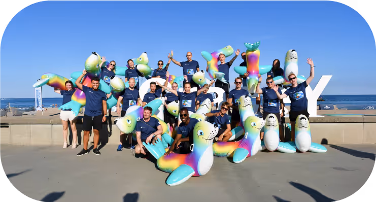 Excited team celebrating outdoors with inflatable seals at a company event by the sea.