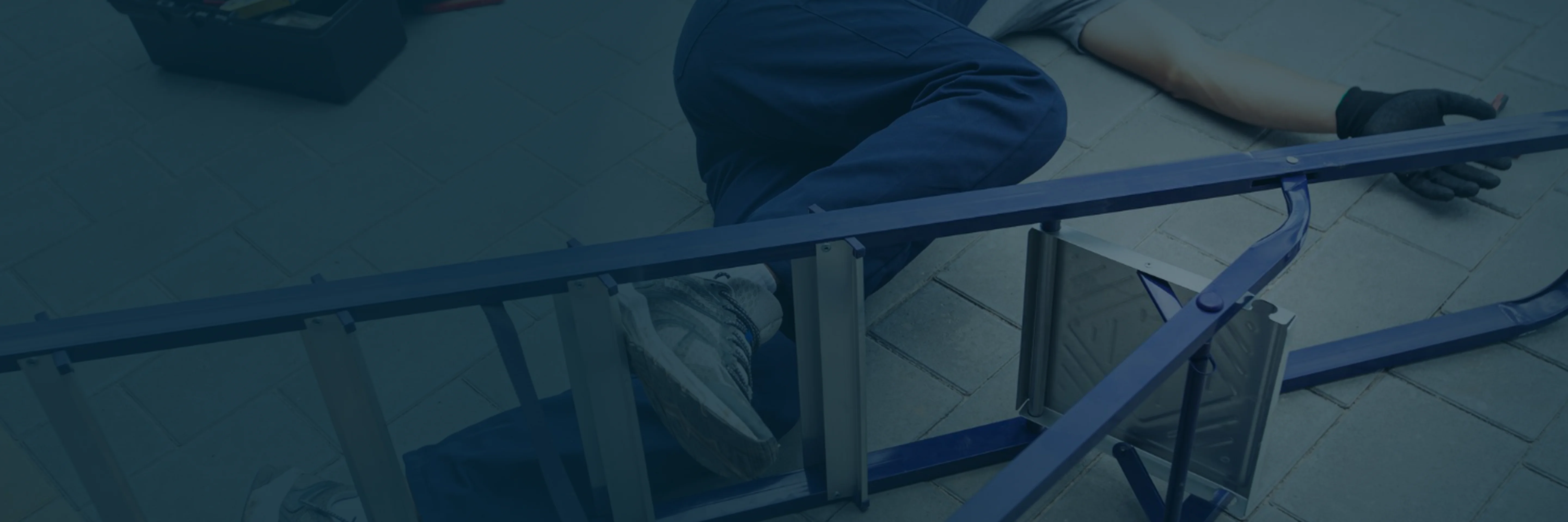 Person lying on the ground next to a metal structure, wearing blue pants, sneakers, and a glove on one hand.